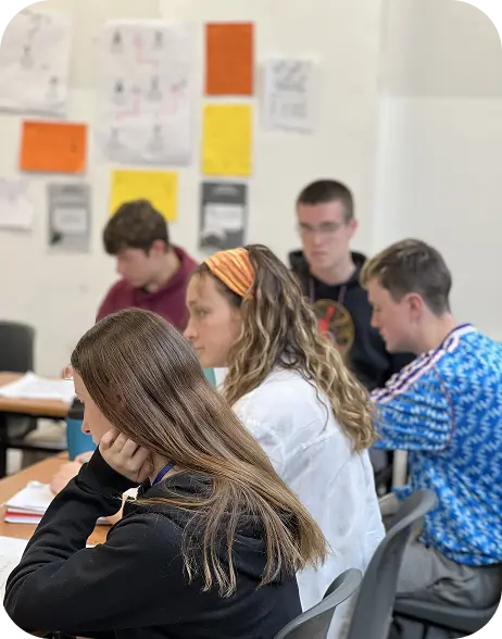 Five students sit at desks in an ELC classroom, focusing on their work. Papers and colourful posters are displayed on the wall in the background, creating a studious and collaborative atmosphere.